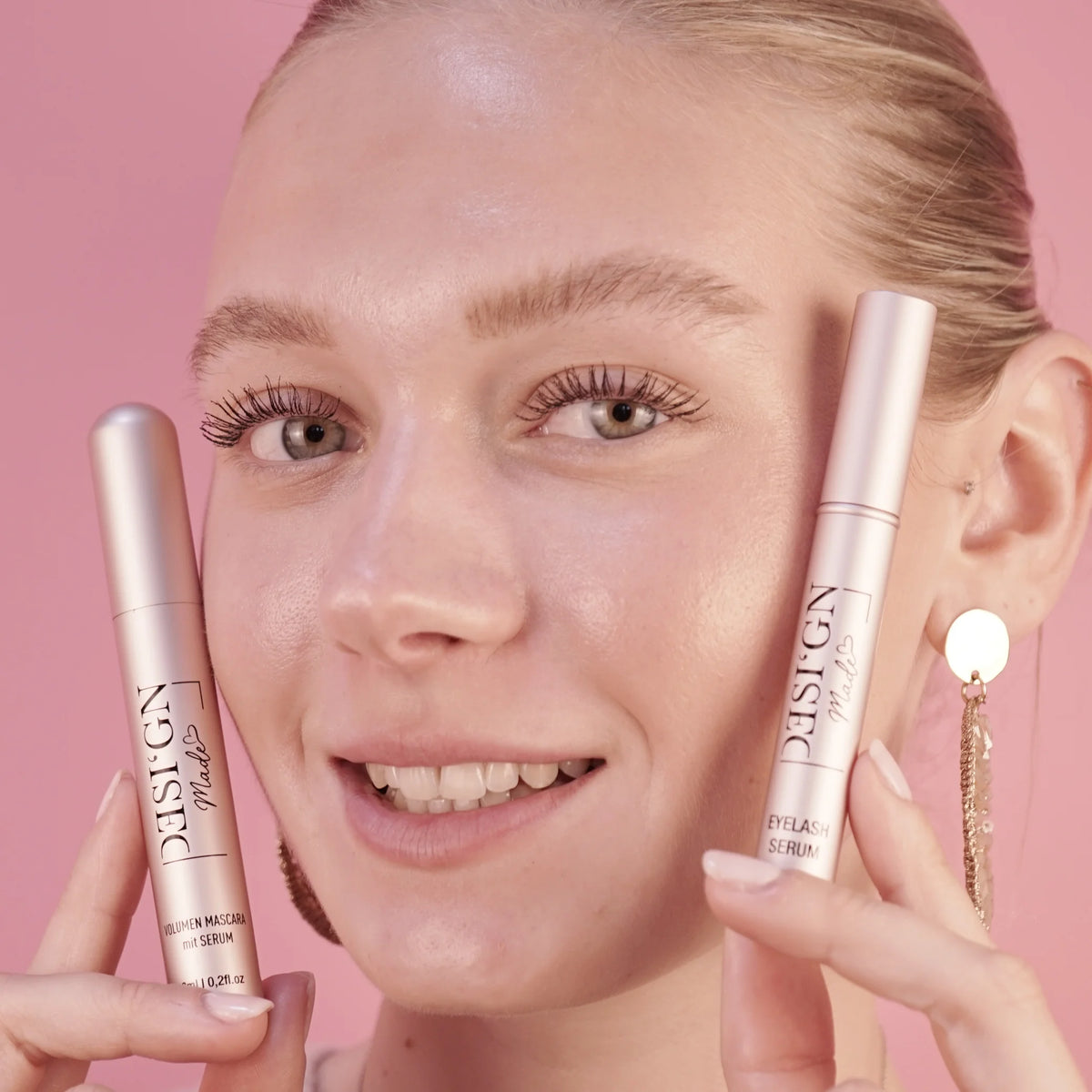 Frau hält die VOLUMEN MASCARA und das EYELASH SERUM von DESI'GN MADE neben ihr Gesicht