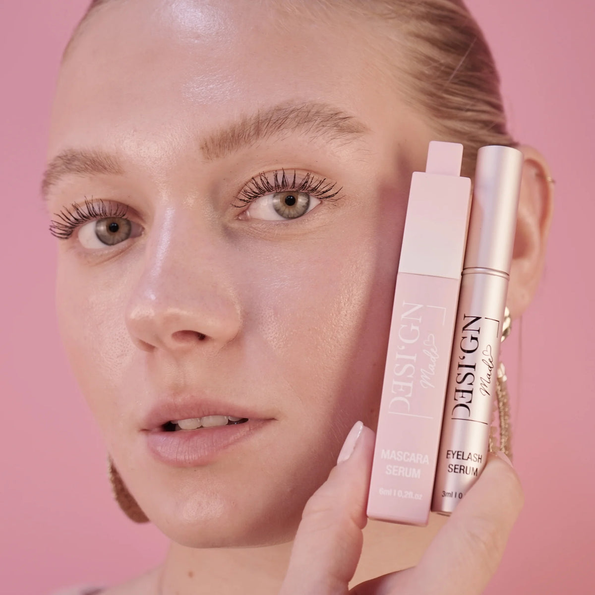 Frau hält die Tuben MASCARA SERUM und EYELASH SERUM von DESI'GN MADE neben ihr Gesicht