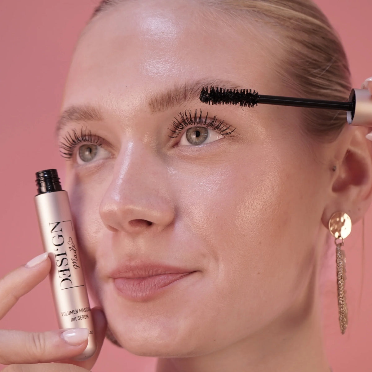 Frau trägt die TUBING VOLUMEN MASCARA von DESI'GN MADE mit der Bürste auf die oberen Wimpern auf und hält die Tube in der Hand