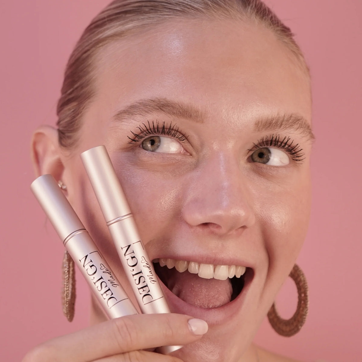 Lachende Frau hält zwei roségoldene Serum-Tuben von DESI'GN MADE vor ihr Gesicht